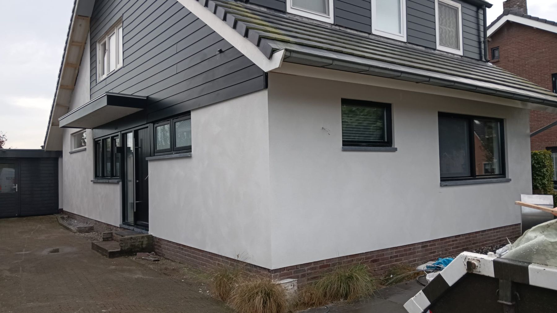 Vrijstaande woning met een wit gestucte benedenverdieping en donkere gevelbekleding erboven