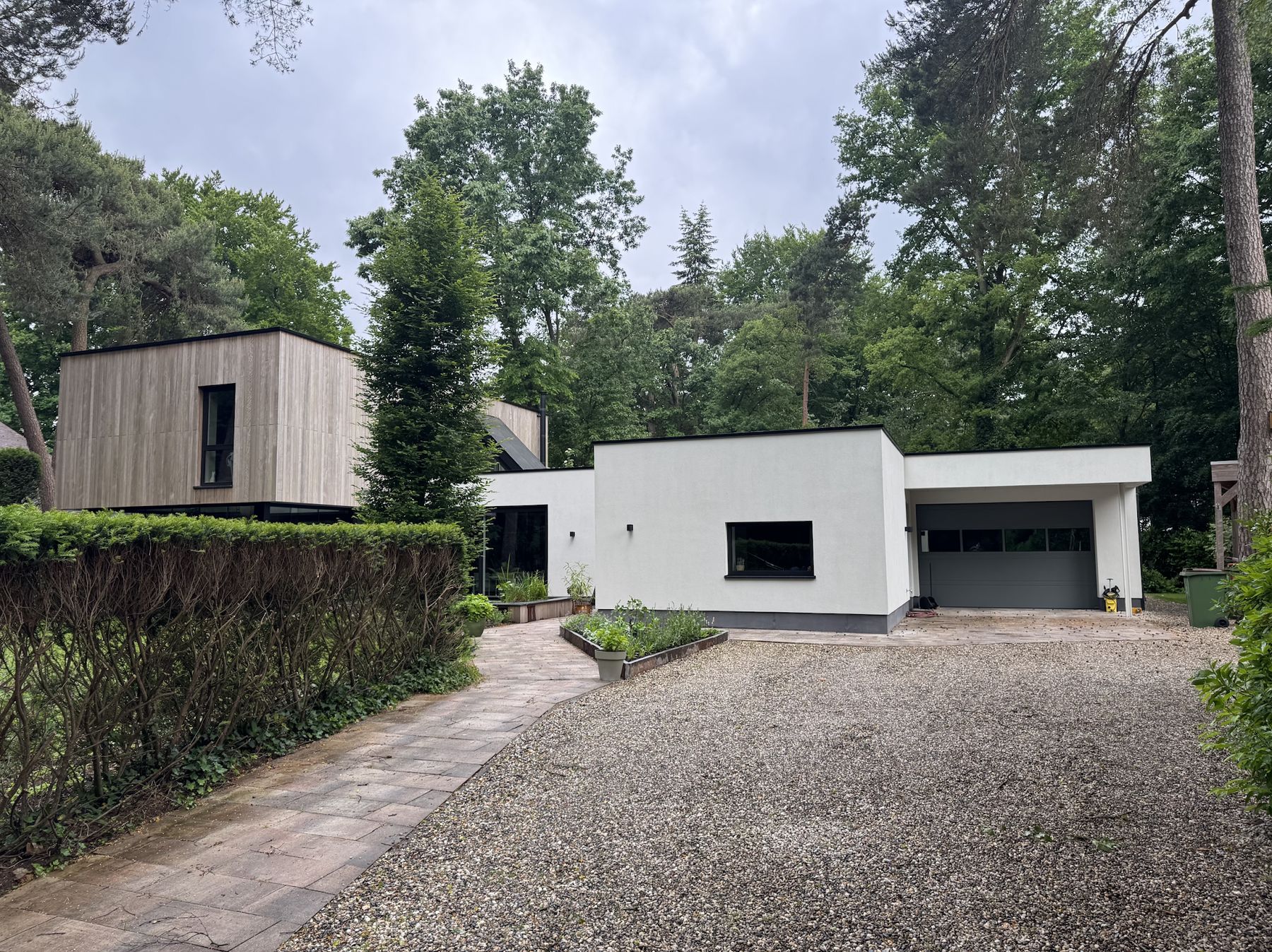 Herbouwde woning met wit gestucte vleugel, garage en houten volume, gezien vanaf de oprit
