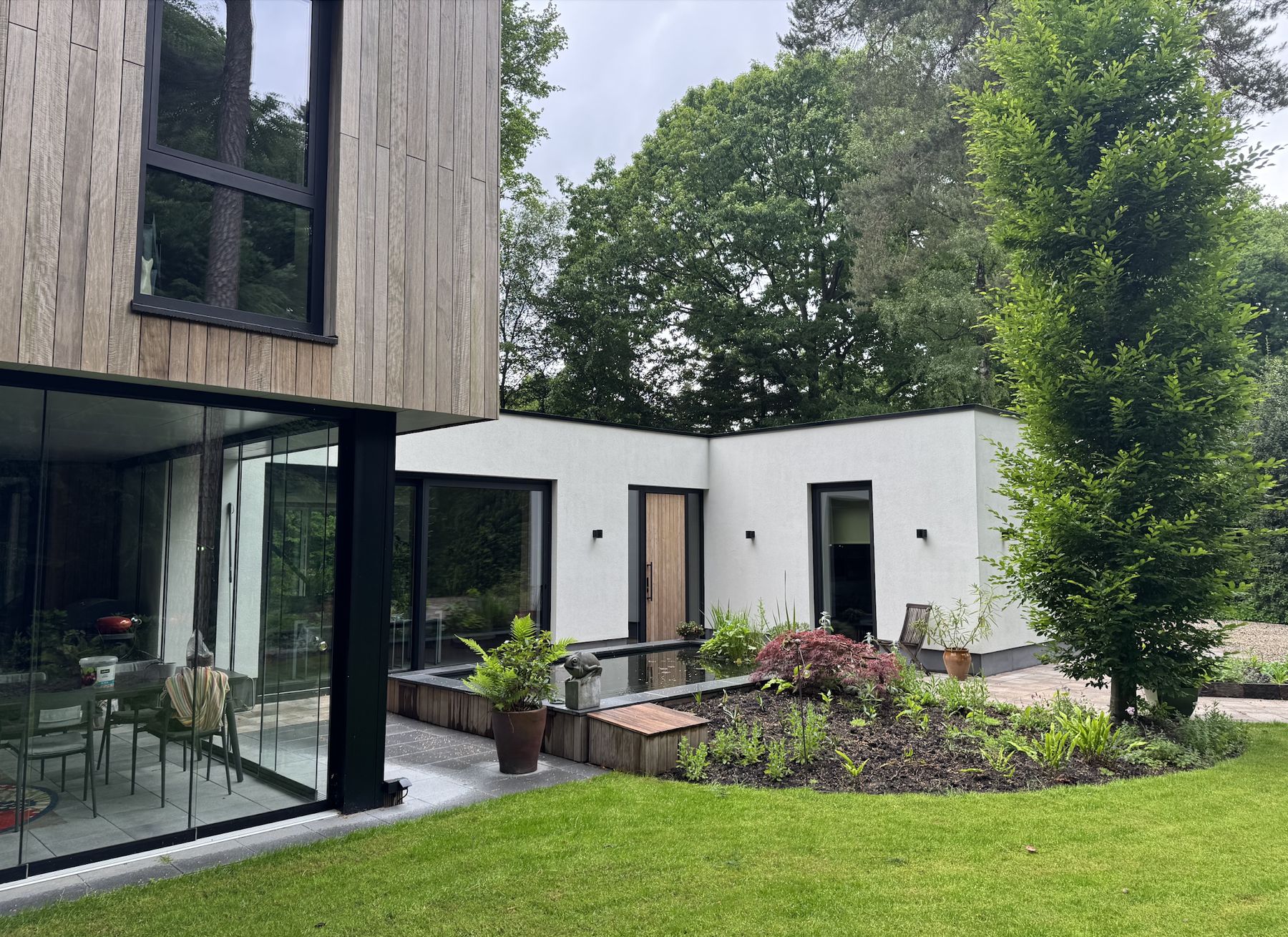Achterzijde van de woning: glazen tuinkamer, wit gestucte vleugel en tuin